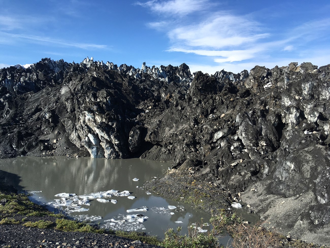 glacial debris, dirt-covered, jagged snow and ice with a pool of murky water nearby
