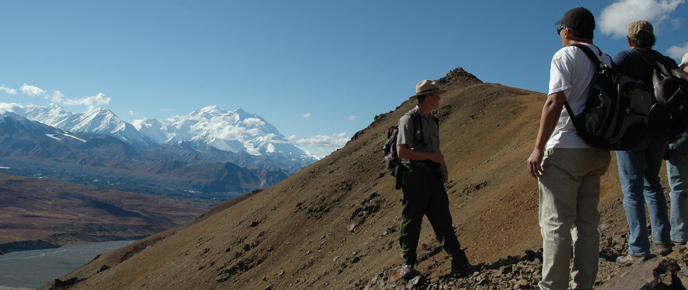 A ranger and hikers on an alpine ridge, Denali in the background