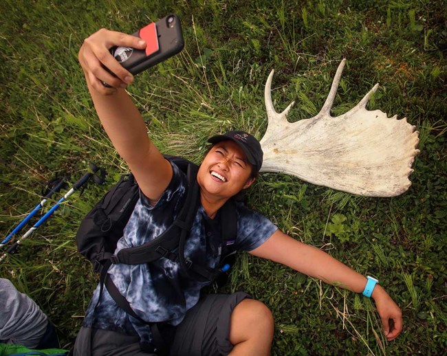 a woman laying on the ground taking a selfie next to a moose skull