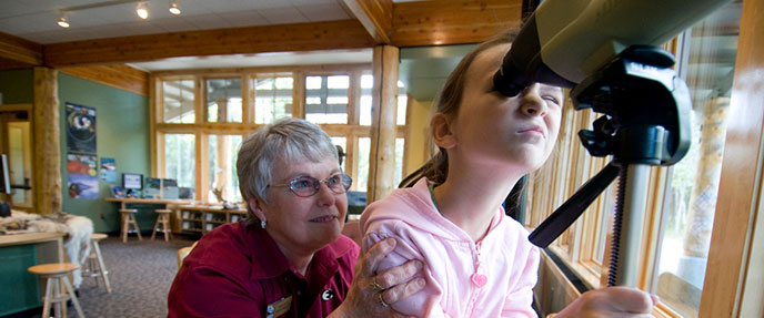 Woman in Alaska Geographic uniform helps young girl look through a spotting scope