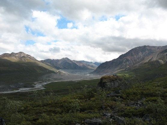 a wide valley with a shallow river in the middle, surrounded by grey, rocky mountains