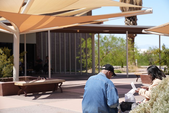 Couple eating lunch on bench in shade at Furnace Creek Visitor Center Courtyard