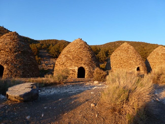 Beehive shaped charcoal kilns made of rock line a forested mountain road.