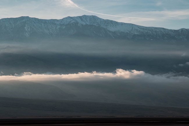 Fog lingers across desert mountains dusted with snow.