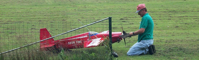 A large model airplane in a field with a man tending to it