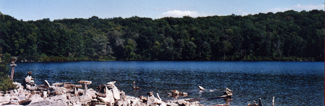 A large lake with forest on the far shoreline and rocks on the near shoreline