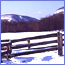A mountain seen across a snowy field and a rail fence