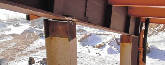 The tops of steel columns welded to a roofing structure with the snow-covered ground visible far below. 