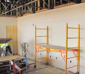 A work scaffold/ladder sits in front of a wall with newly installed drywall. 