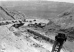 Low walls, recently built, mark the outline of the quarry, with construction equipment and workmen in scene. 