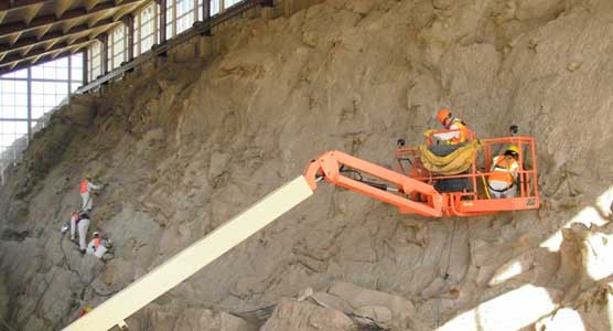 Staff from Dinosaur NM, standing on the quarry face and in a man-lift,  clean the quarry with vacuums, removing dust and dirt accumulated during construction.