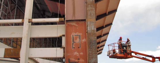 Two men in a lift prepare to work on structural steel near the roofline of the exhibit hall. 