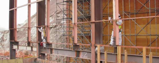 Two people in white work on lead paint abatement on steel columns painted pink. 