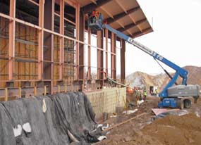 A wall under construction is partly covered with blankets & a person in a man-lift works on lead paint abatement at the top of a steel column. 