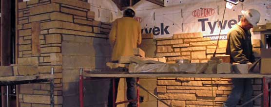 Two stone masons work on the stone veneer inside the Quarry Visitor Center. 