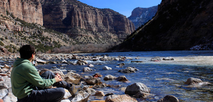 A hiker rests along the Green River at Jones Hole.
