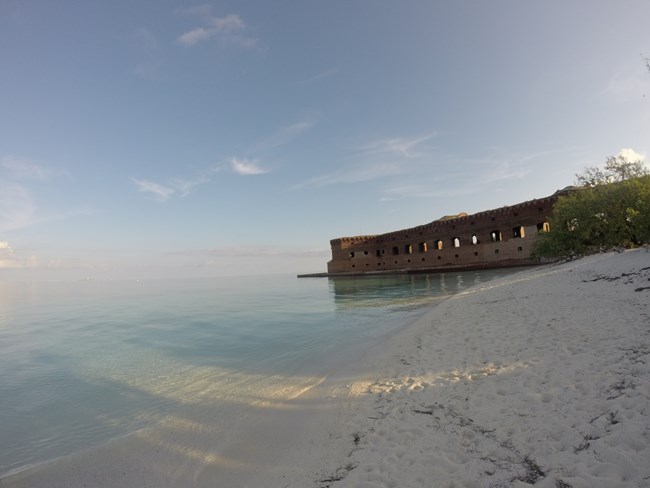 A sandy beach at sunset with a large brick fort behind it