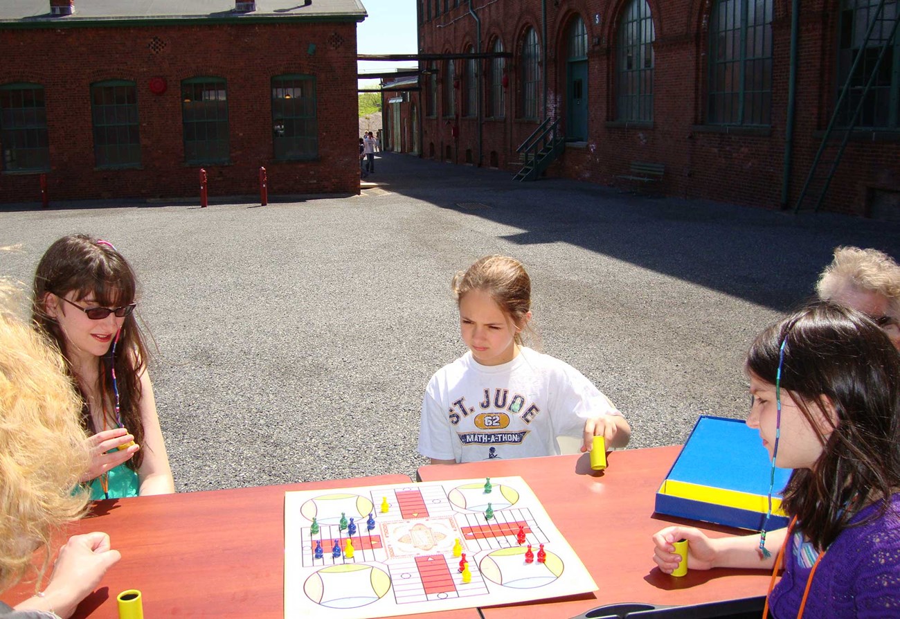 Children sitting around a table playing Edison's favorite game, Parcheesi.