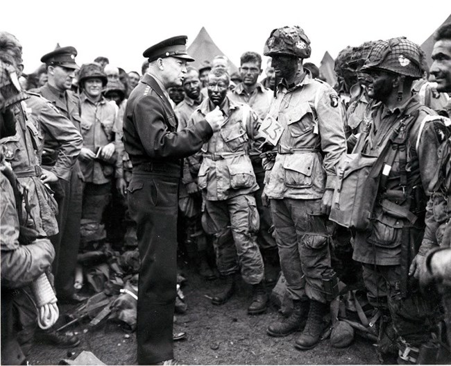 Black and white image of General Eisenhower speaking to a group of paratroopers in uniform