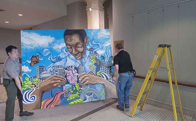 NPS Ranger Peter Wong and NPS Museum Technician Brent Talbot work to install one of the six Groundswell murals for a special exhibition at Ellis Island.