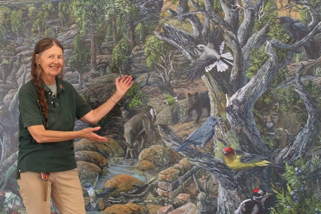 An El Malpais volunteer stands in front of a mural depicting wildlife in the area