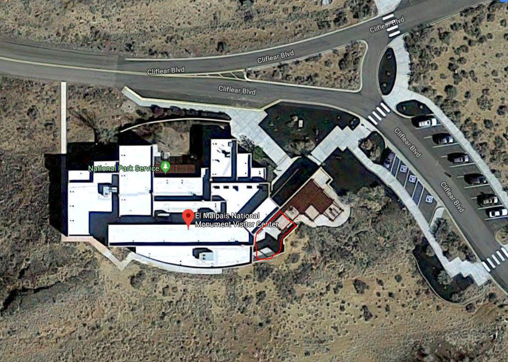 A satellite view of a large white building with a road and parking area, showing a location circled in red.