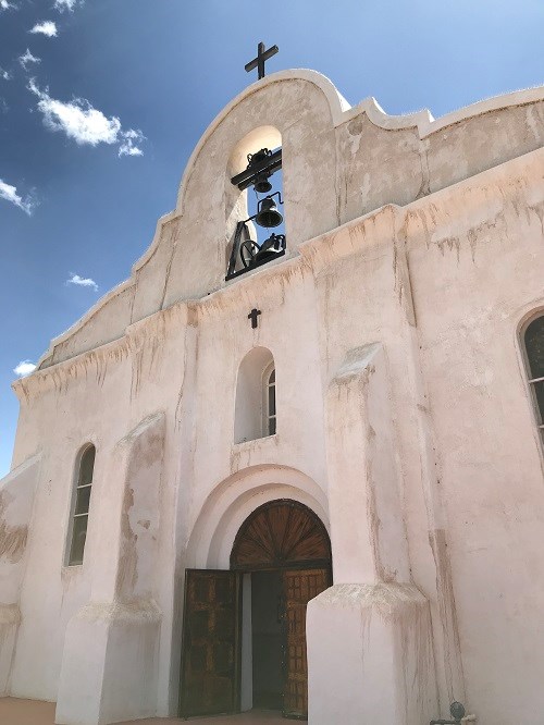 front of white chapel, old spanish style, with cross at the top, and a bell centered
