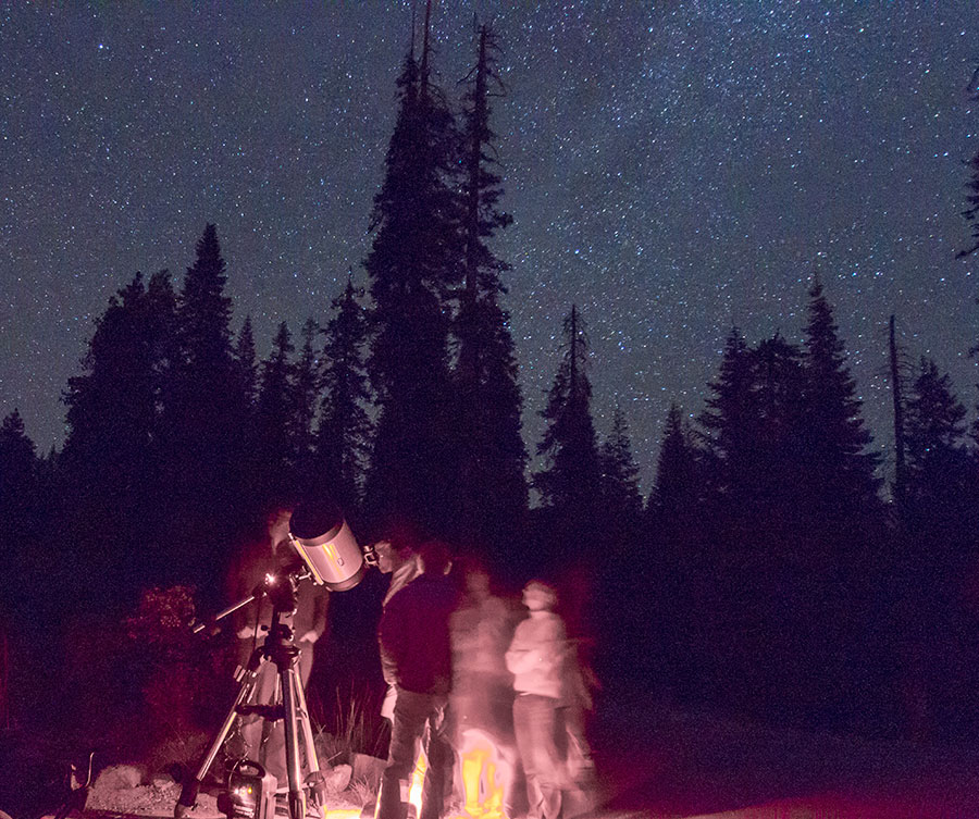 A night photo of people with a telescope under a starry sky