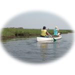 Two paddlers float on calm water beside the salt marsh.