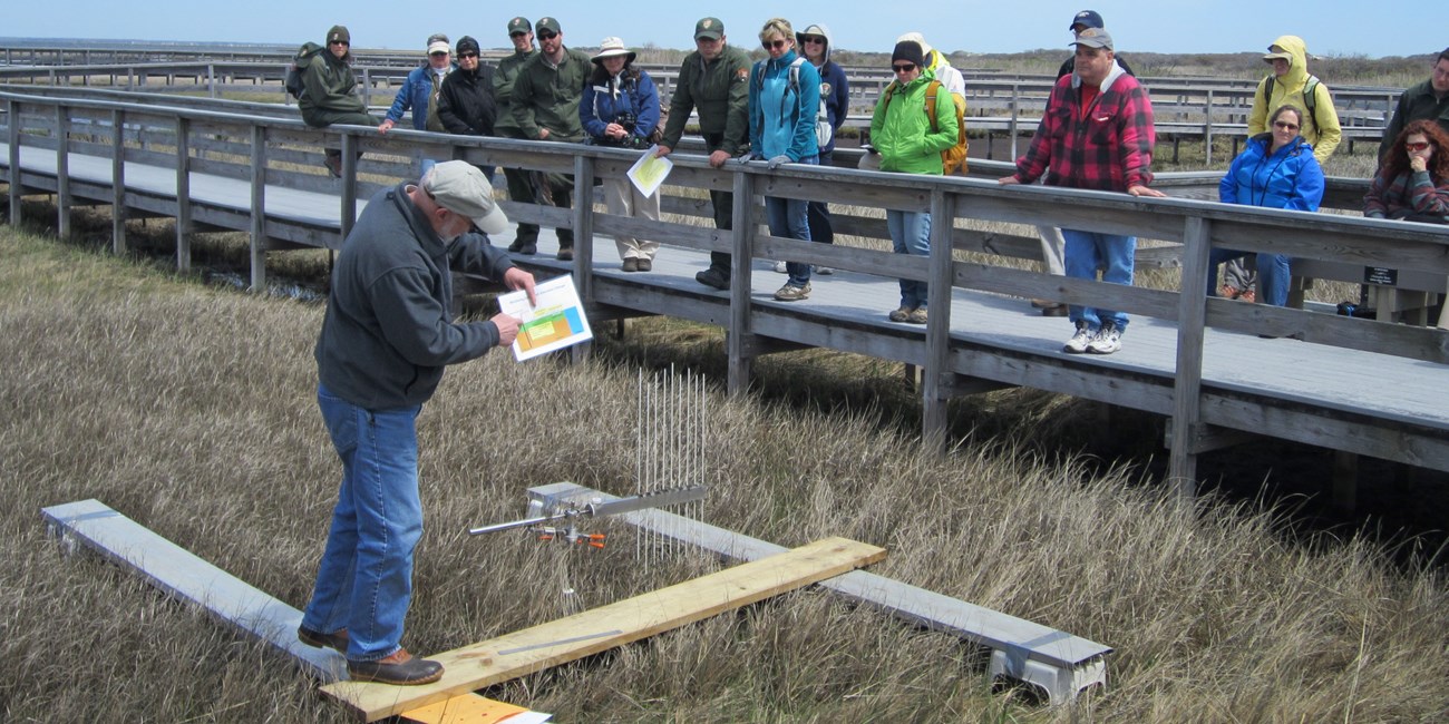 Dr. Charles Roman presents nest to a Surface Elevation Table (SET), an instrument used to monitor changes in salt marsh elevation.