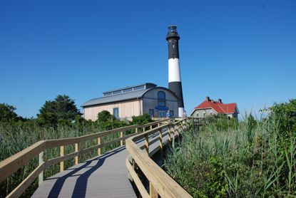 Boardwalk leads to new Fresnel Lens Building with Fire Island Lighthouse and its keepers quarters beyond.