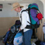 Man dressed in light-colored clothing, wearing large backpack, loads gear onto ferry.