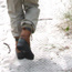 With pants tucked inside boots, person walks past beach grass.