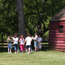 Group gathers under tree near red barn.