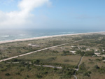 Aerial view of boardwalks meandering from a large parking lot, ocean waves in the background.