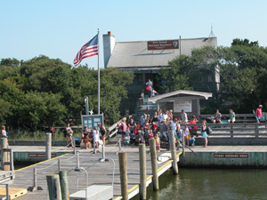 View of passengers waiting on dock in front of visitor center, surrounded by lush shrubby trees.