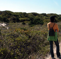 Woman stands on trail with grasses and shrubs nearby.