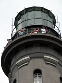 Lighthouse tower tour participants stand along rail of gallery near the top of the Fire Island Lighthouse, under the glass-enclosed lantern room and within the uppermost black daymark of the structure. Lighthouse tower tour participants stand along rail of gallery near the top of the Fire Island Lighthouse, under the glass-enclosed lantern room and within the uppermost black daymark of the structure.