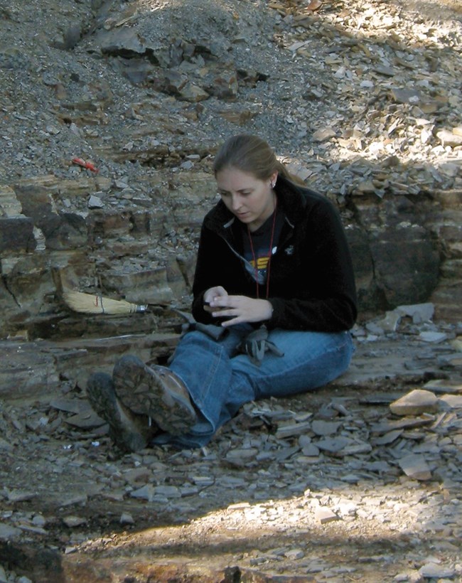 a woman looking at a shale fossil while conducting field work