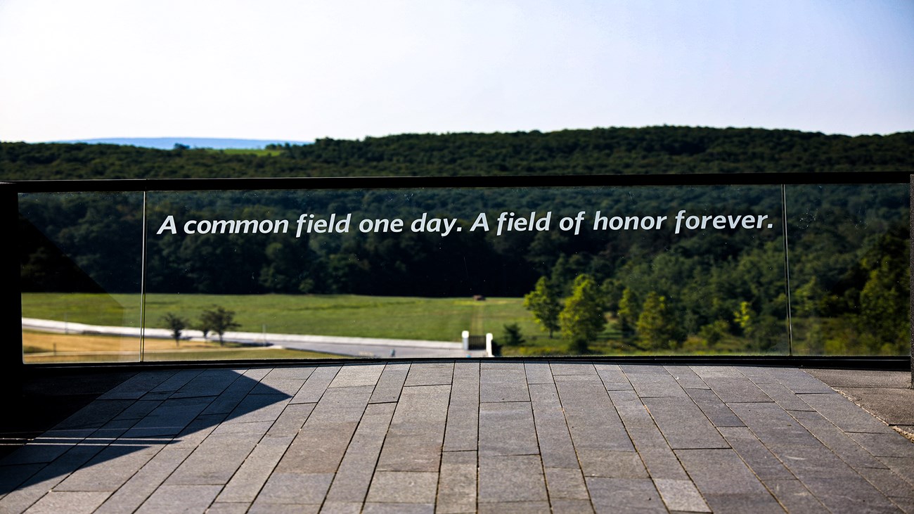 A glass panel that reads "A common field one day. A field of honor forever" overlooks the wall of names and crash site.