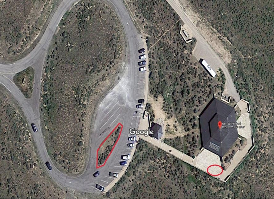 An aerial view of the visitor center on the right and parking lot on the left.  There is a red circle around a location near the visitor center front doors and around the island in the parking lot.