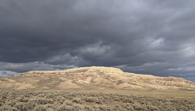 Grey clouds above a butte with sagebrush in the foreground.