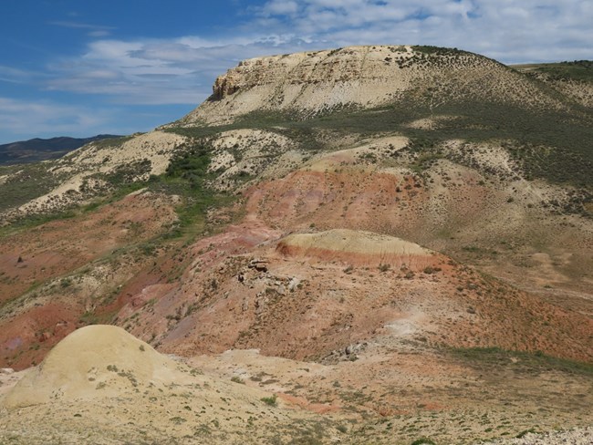 A hill topped with white sediments with ledges of the Fossil Butte Member visible on the side. Red and purple hills of the Wasatch Formation are in the foreground.