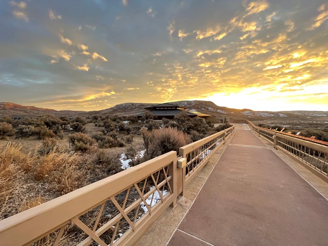 A ramp leading down to a building with the sun rising behind Fossil Butte.