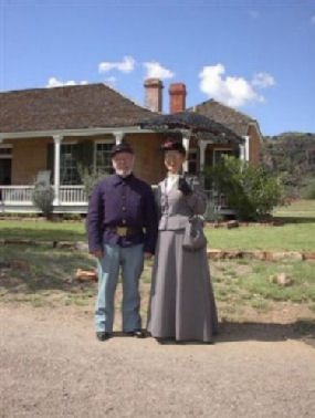 A volunteer couple posing in 1880's period clothing in front of the Commanding Officer's Quarters.