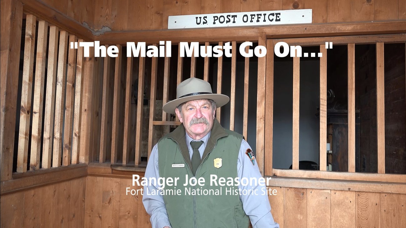 Ranger Joe reasoner standing in front of the wooden bars of the 1800s post office at Fort Laramie.