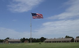 U.S. flag on tall flag pole.  Two sandstone buildings in background on either side of flagpole.