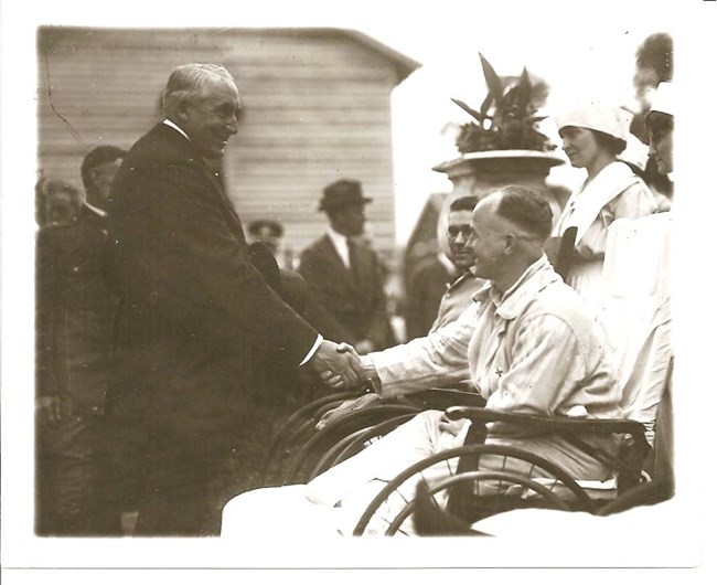 A black and white image of Warren G. Harding shaking hands with a soldier in a wheelchair.