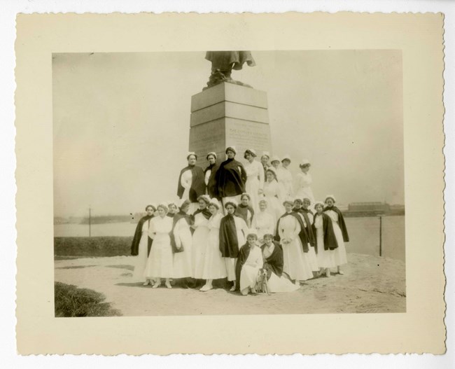 A black and white image of a group of nurses at the base of the George Armistead statue.