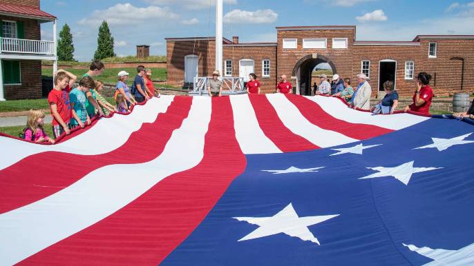 Visitors hold the edges of the 30-by-42 foot Star-Spangled Banner replica flag